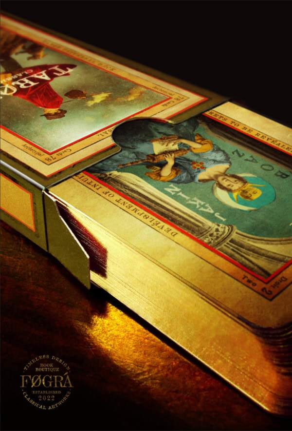 A close-up of a deck of tarot cards with gold edges partially removed from a box, showing detailed illustrations and vintage-style design. The cards are upside down, and the box has ornate text and decorative elements.