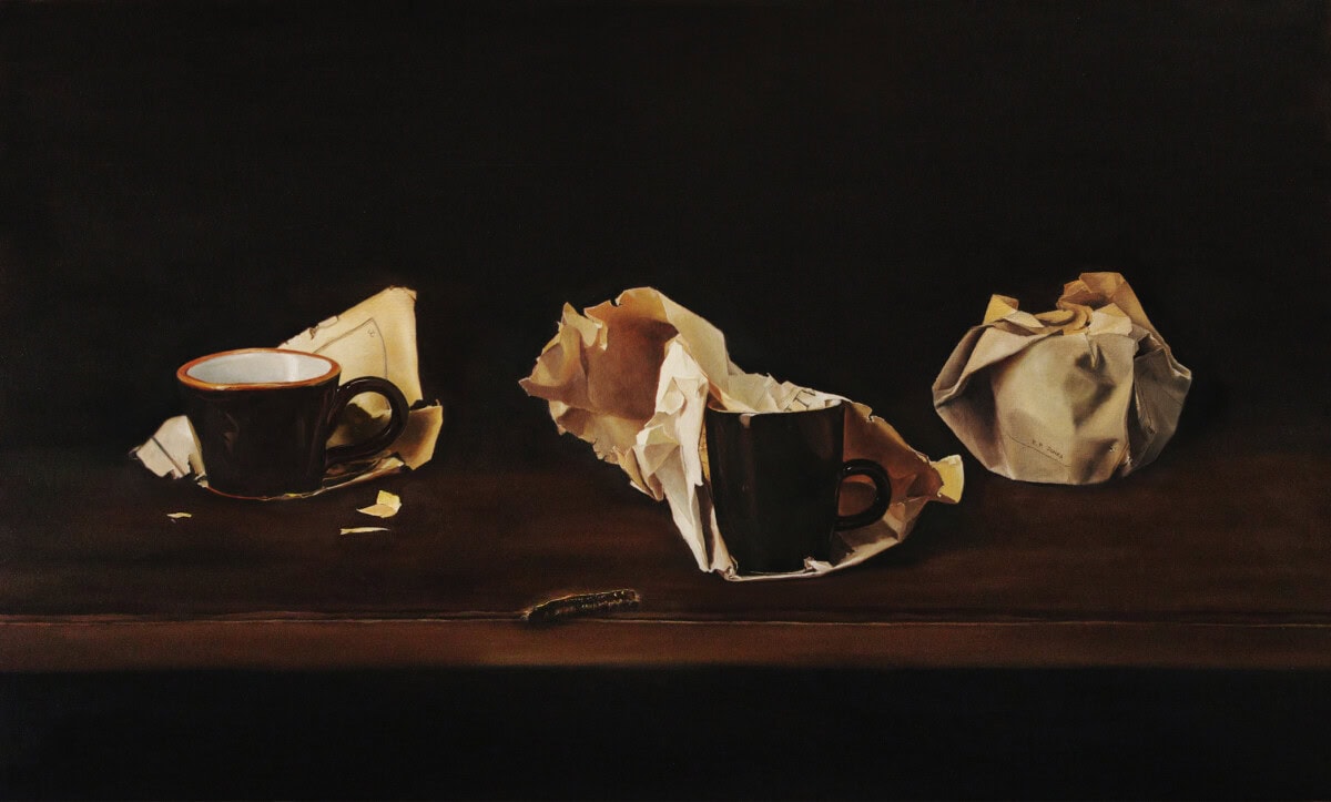 Two dark ceramic cups sit among crumpled pieces of brown and white paper on a dark wooden surface, with a small caterpillar crawling in the foreground. The background is black, highlighting the still life arrangement.
