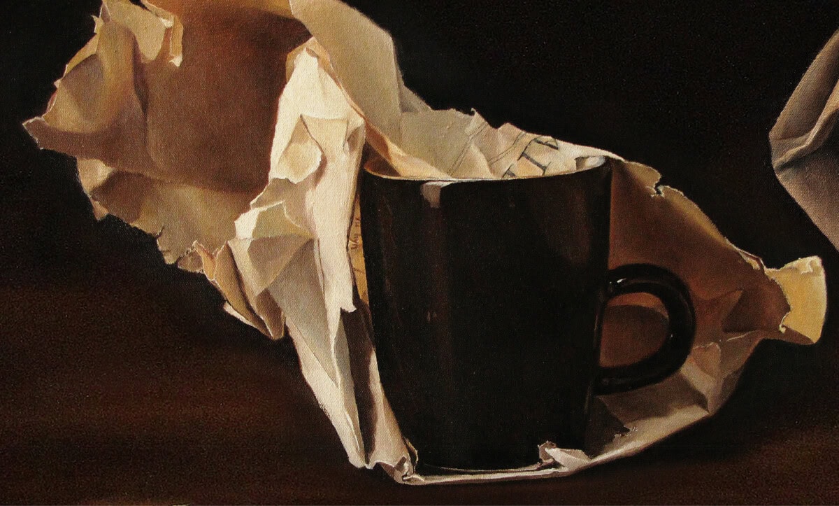 A black ceramic mug partially wrapped in crumpled brown paper sits on a dark surface, with dramatic lighting highlighting the cup and textured paper.